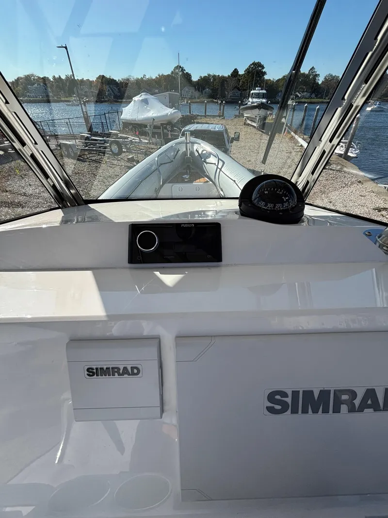 Slide: The Image of 2024 Protector 330 Chase boat dashboard with Simrad equipment, docked by a scenic waterfront. - 8