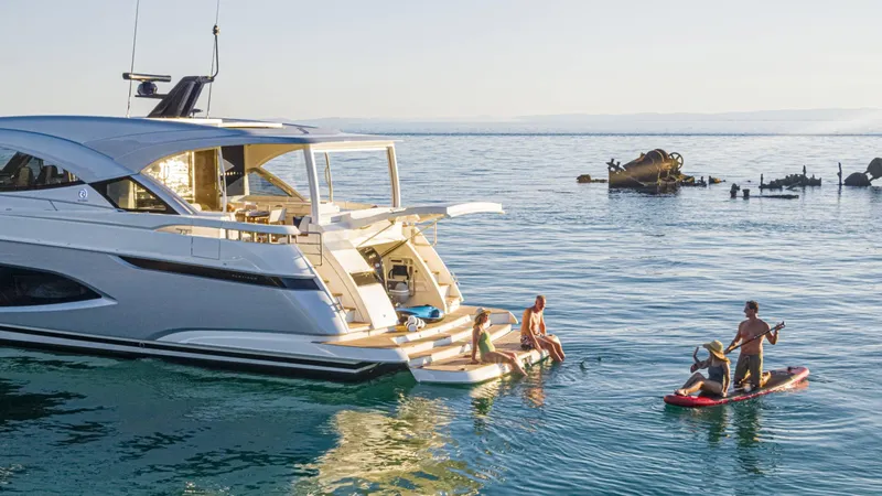 Slide: The Image of 2025 Riviera 6800 Sport Yacht Platinum Edition with people enjoying water activities nearby. - 15