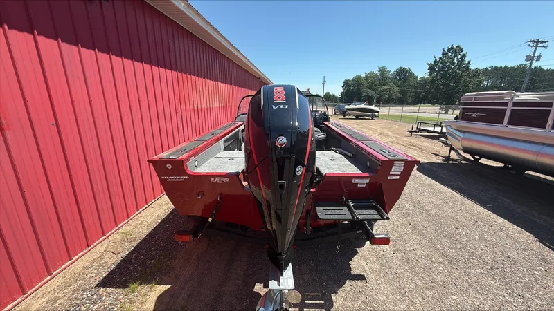 Slide: The Image of 2025 Tracker Targa V-19 Combo boat with powerful outboard motor, parked near a red building. - 2