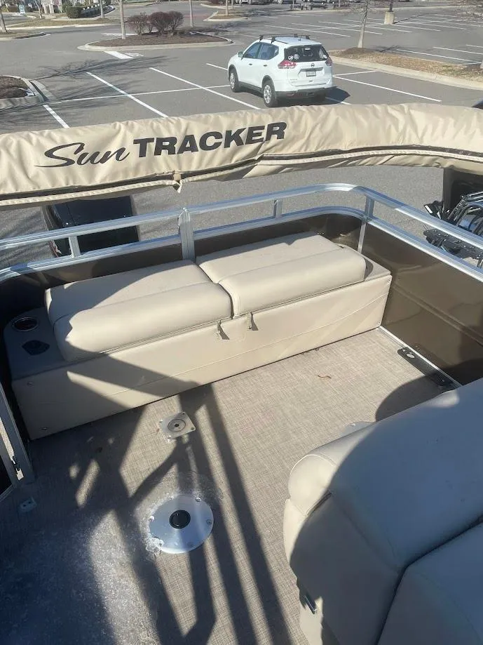 Slide: The Image of 2025 Sun Tracker SportFish 22 DLX pontoon boat interior with beige seating in a parking lot. - 3