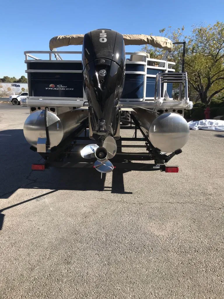 Slide: The Image of 2025 Sun Tracker Fishin' Barge 22 DLX pontoon boat, rear view, parked outdoors. - 2