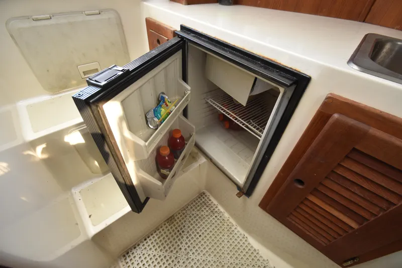 Slide: The Image of 1999 Carolina Classic 28 Express boat interior with open mini fridge and storage compartments. - 19