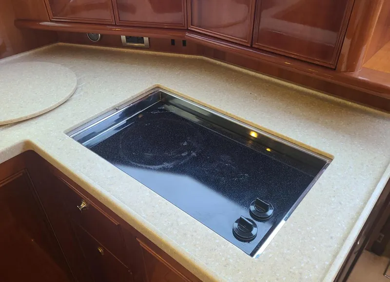 Slide: The Image of 2009 Riviera 47 Enclosed Flybridge Series II yacht kitchen with sleek stovetop and wooden cabinetry. - 25