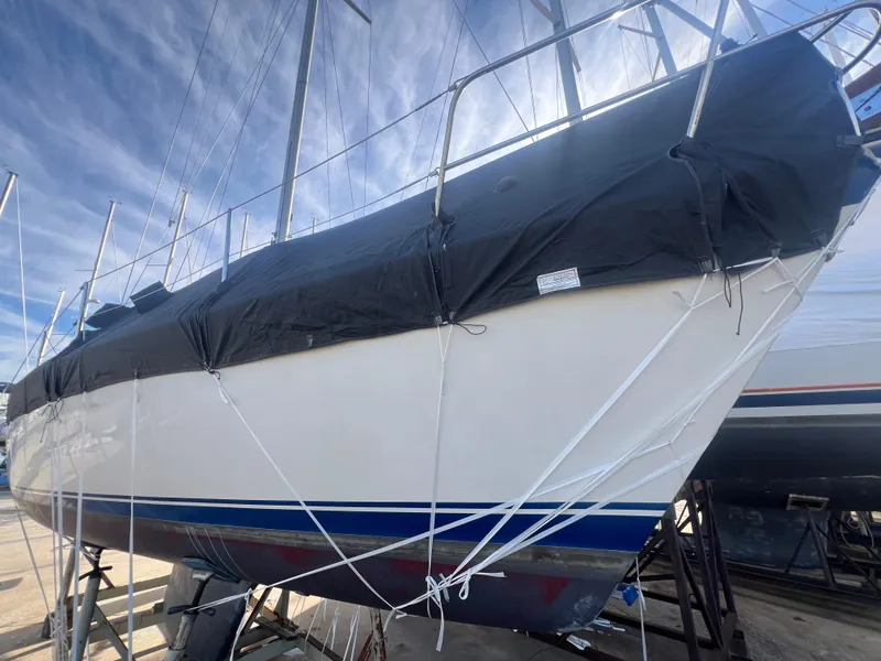 Slide: The Image of 1983 O'Day 34 sailboat with black cover, docked on land under a blue sky. - 39