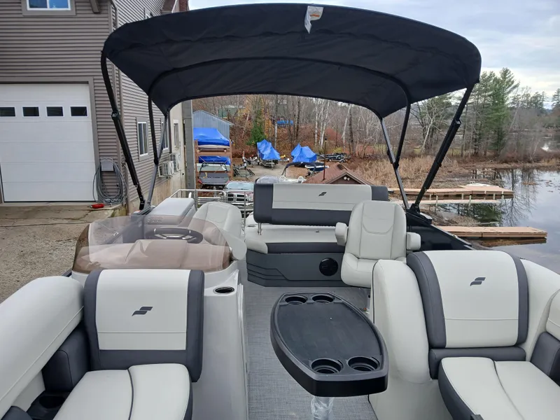 Slide: The Image of 2025 Starcraft EXS 1 Q DH pontoon boat with canopy, docked near a lakeside house. - 2