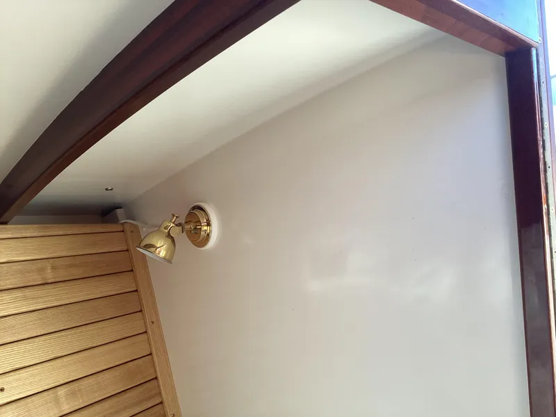 Slide: The Image of Interior of 2024 MacKenzie Cuttyhunk boat with wooden paneling and brass light fixture. - 19