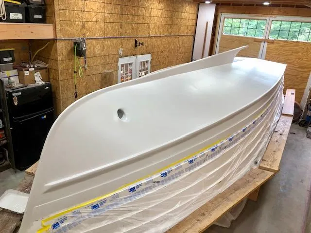 Slide: The Image of 2024 MacKenzie Cuttyhunk boat hull in workshop, partially covered with protective plastic. - 36
