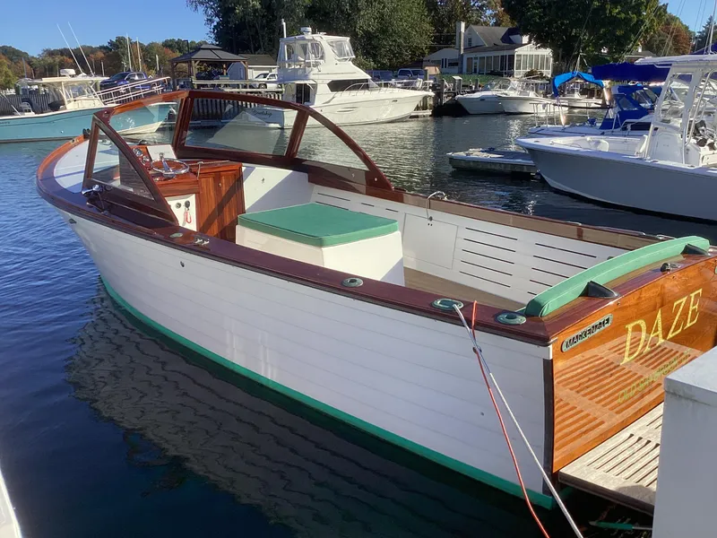 Slide: The Image of 2024 MacKenzie Cuttyhunk boat docked in marina, featuring wooden accents and green trim. - 4