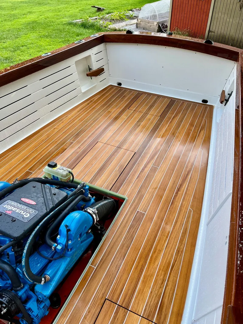 Slide: The Image of 2024 MacKenzie Cuttyhunk boat with wooden deck and visible engine, docked on grass. - 48