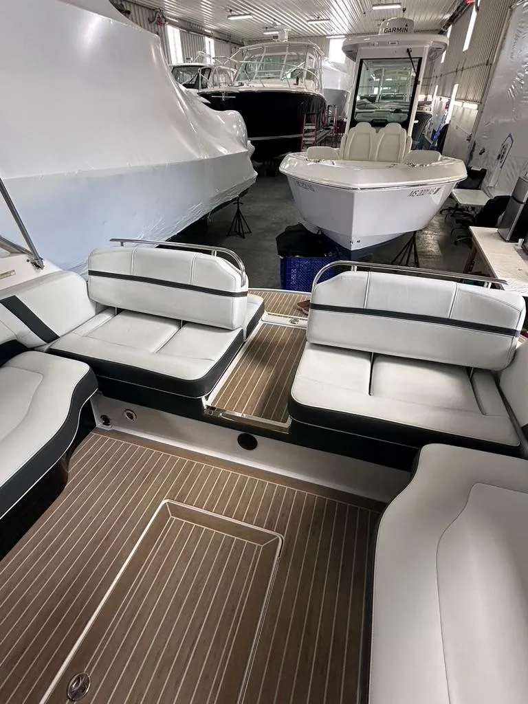 Slide: The Image of 2015 Regal 2800 Bowrider interior with white seating and wood flooring in a showroom. - 13