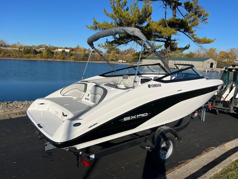 Slide: The Image of 2025 Yamaha Boats SX190 on trailer by a lake, under clear blue sky. - 5