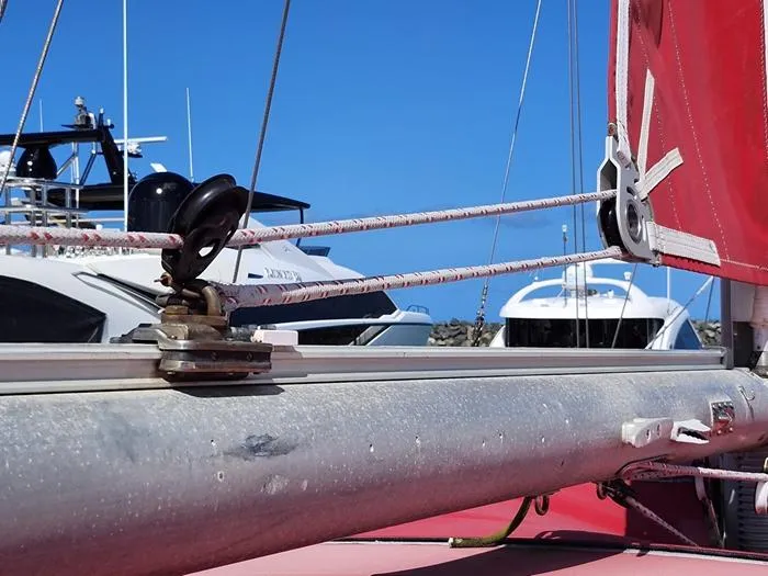 Slide: The Image of Close-up of 1983 Morgan Schooner rigging with red sail and boats in background. - 24