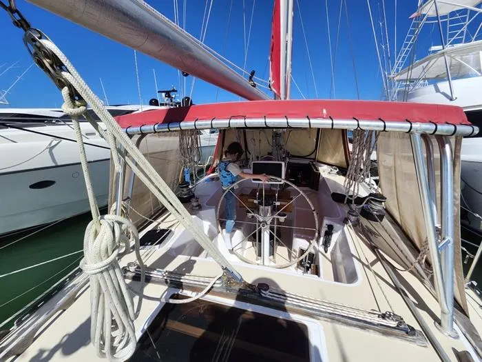 Slide: The Image of 1983 Morgan Schooner sailboat with red canopy docked at marina, clear blue sky. - 36