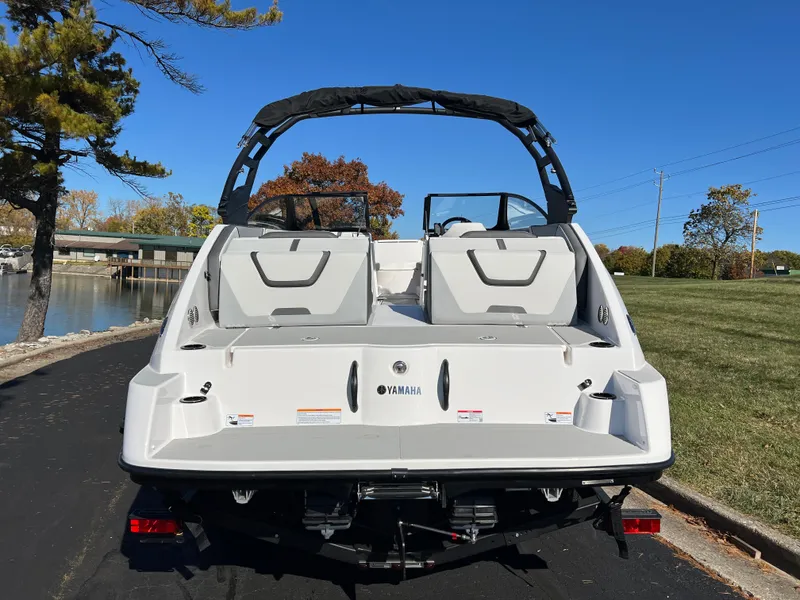 Slide: The Image of 2025 Yamaha Boats AR220, rear view, parked near a lake under clear blue sky. - 6