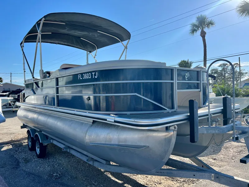 Slide: The Image of 2023 Cypress Cay Seabreeze 232 pontoon boat on trailer, sunny day, palm trees in background. - 1