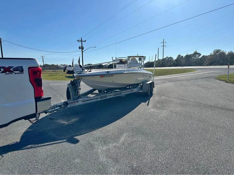 Slide: The Image of 2005 Young Boats 20 on trailer, hitched to a white truck, parked on a sunny road. - 1