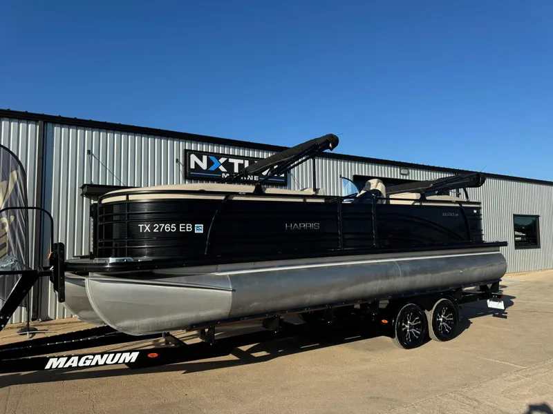 Slide: The Image of 2018 Harris Solstice 240 pontoon boat on a trailer outside a marine dealership. - 1