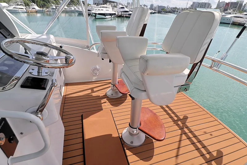 Slide: The Image of 2004 Hatteras 54 Convertible yacht helm with white captain chairs and wooden deck. - 25