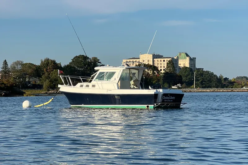 Slide: The Image of 2003 Albin 28 TE Flush Deck boat on calm water near shoreline buildings. - 2