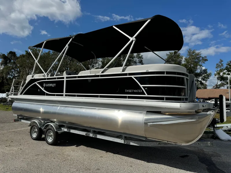 The Image of 2025 Sweetwater 2286 SB pontoon boat with black canopy on a trailer. - 1