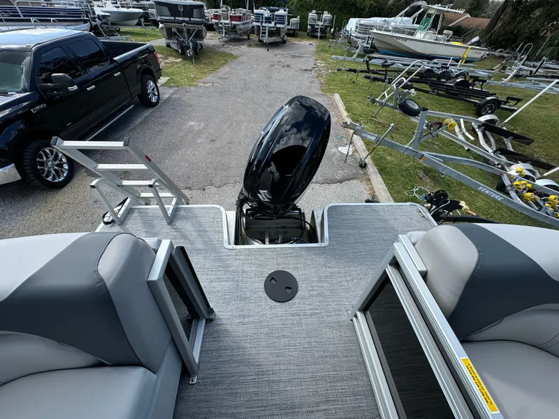 Slide: The Image of 2025 Sweetwater 2286 SB pontoon boat with outboard motor, parked near trailers and a truck. - 10