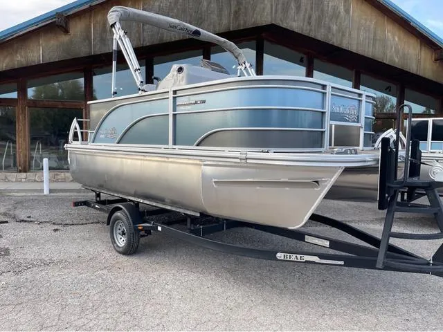Slide: The Image of 2023 SunCatcher Select 16F pontoon boat on trailer, parked outside a wooden building. - 1