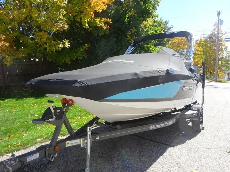 Slide: The Image of 2019 MasterCraft NXT20 boat on trailer with cover, parked on a sunny street. - 3