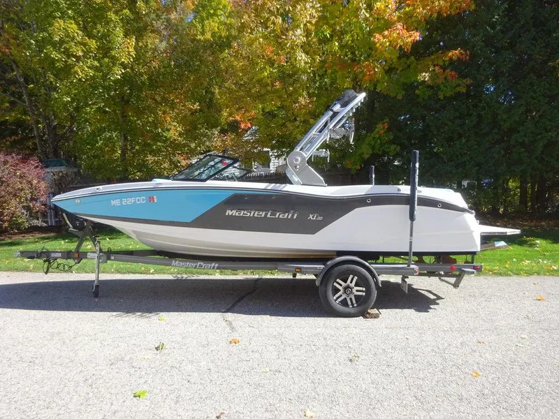 Slide: The Image of 2019 MasterCraft NXT20 boat on trailer, parked outdoors with autumn foliage background. - 4