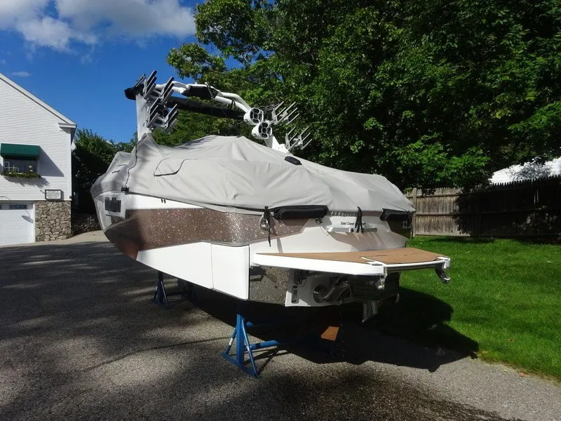 Slide: The Image of 2020 Malibu M240 boat covered and elevated on stands in a driveway. - 3