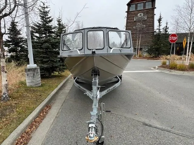 Slide: The Image of 2024 Spartan 185 Astoria boat on trailer, parked on a road near trees and a building. - 8