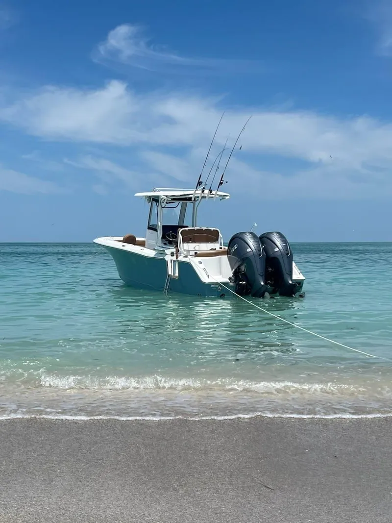 Slide: The Image of 2024 Sea Hunt Ultra 275 SE boat anchored in clear turquoise water near a sandy beach. - 11