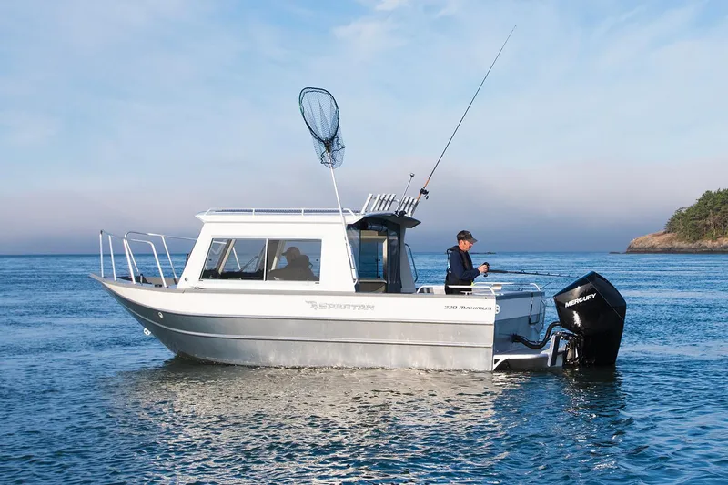 Slide: The Image of 2024 Spartan 220 Maximus boat with Mercury engine on trailer, parked outdoors. - 11