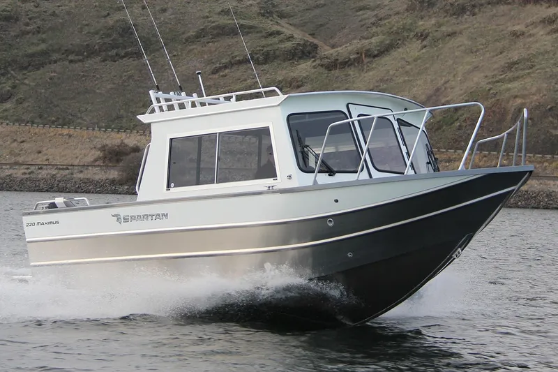 Slide: The Image of 2024 Spartan 220 Maximus boat interior with steering console and storage, parked outdoors. - 14