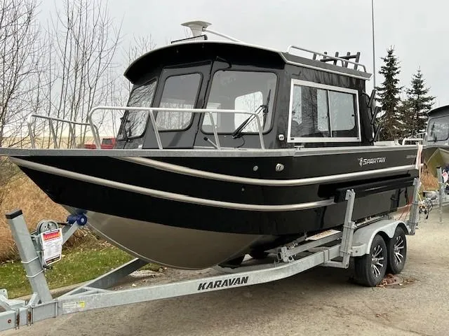 Slide: The Image of 2024 Spartan 220 Maximus boat on trailer, parked on roadside with trees in background. - 2