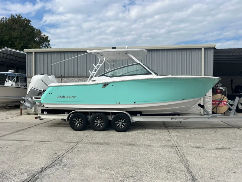 The Image of 2024 Blackfin 272 DC boat on trailer, turquoise hull, parked outside a storage facility. - 0