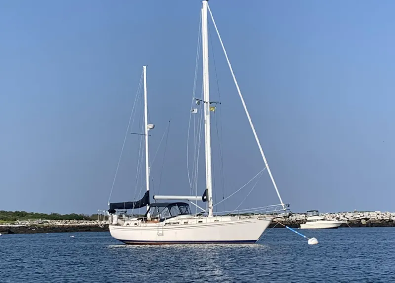 Slide: The Image of 1984 Whitby 42 Ketch sailboat anchored on calm water under clear blue sky. - 10