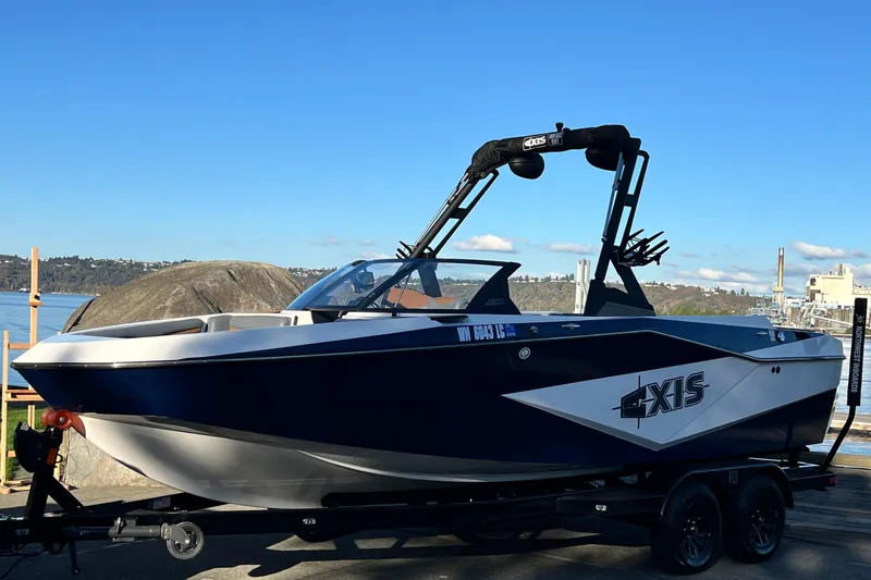 The Image of 2024 Axis T 220 boat on trailer by waterfront, clear sky background. - 0