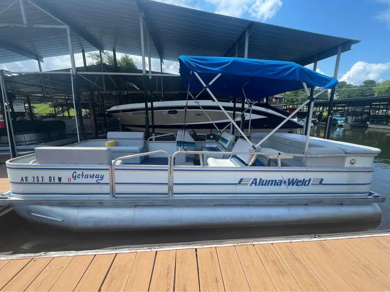 Slide: The Image of 1994 Alumaweld Getaway pontoon boat docked with blue canopy under marina shelter. - 3