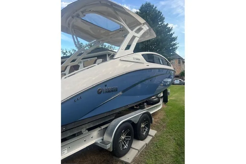Slide: The Image of 2023 Yamaha Boats 275SDX on trailer, blue and white design, parked on grass. - 4