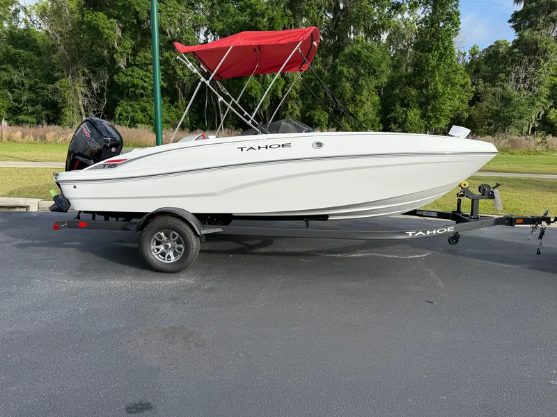 Slide: The Image of 2025 Tahoe T18 boat with red canopy on trailer, parked outdoors. - 3