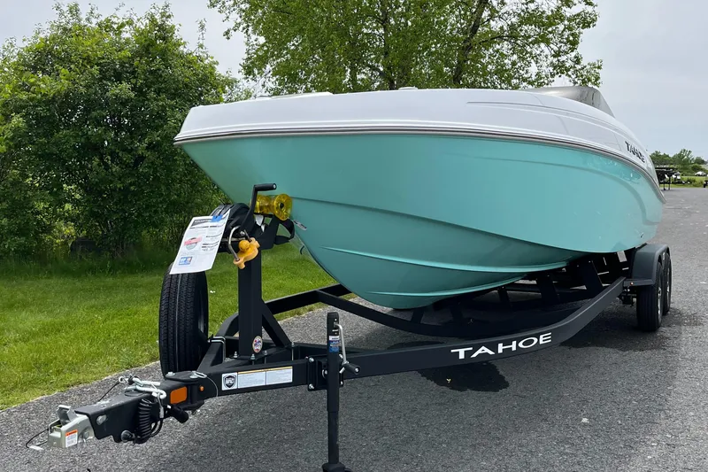 Slide: The Image of 2025 Tahoe T21 boat on trailer, parked on road with greenery in background. - 2