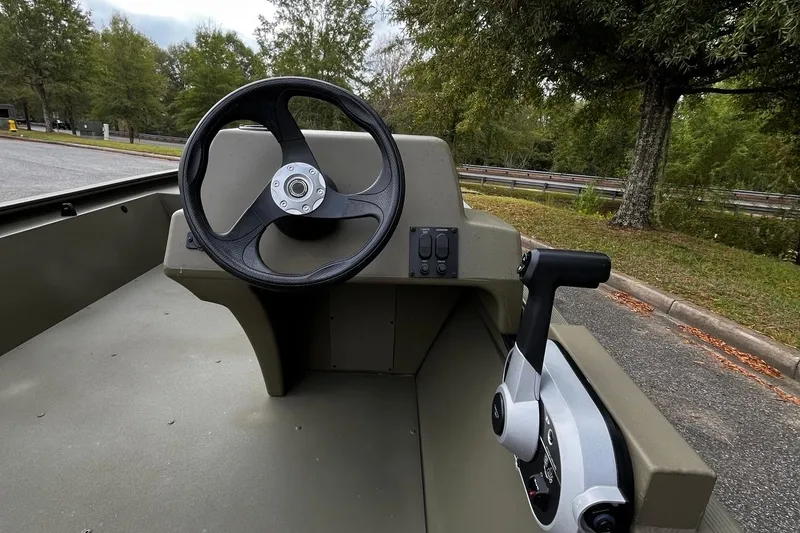 Slide: The Image of 2025 Tracker Grizzly 1648 SC boat steering console with control lever, parked outdoors. - 5