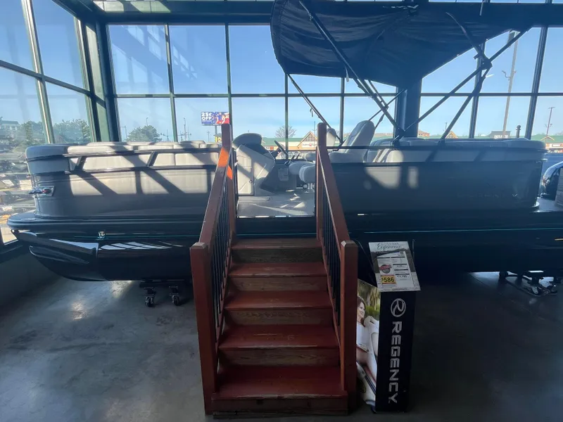 The Image of 2025 Regency 230 DL3 pontoon boat displayed indoors with wooden stairs. - 0