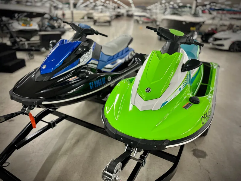 Slide: The Image of Two 2022 Yamaha WaveRunner EX jet skis, blue and green, on display indoors. - 1