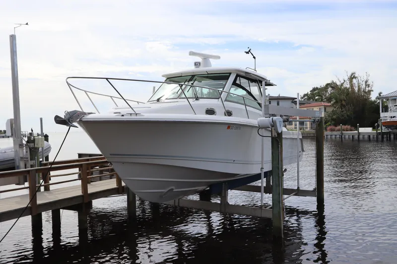 Slide: The Image of 2019 Boston Whaler 315 Conquest boat docked on a lift by the water. - 0