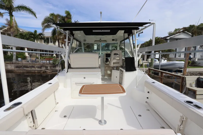 Slide: The Image of 2019 Boston Whaler 315 Conquest boat interior with seating and table, docked by palm trees. - 20