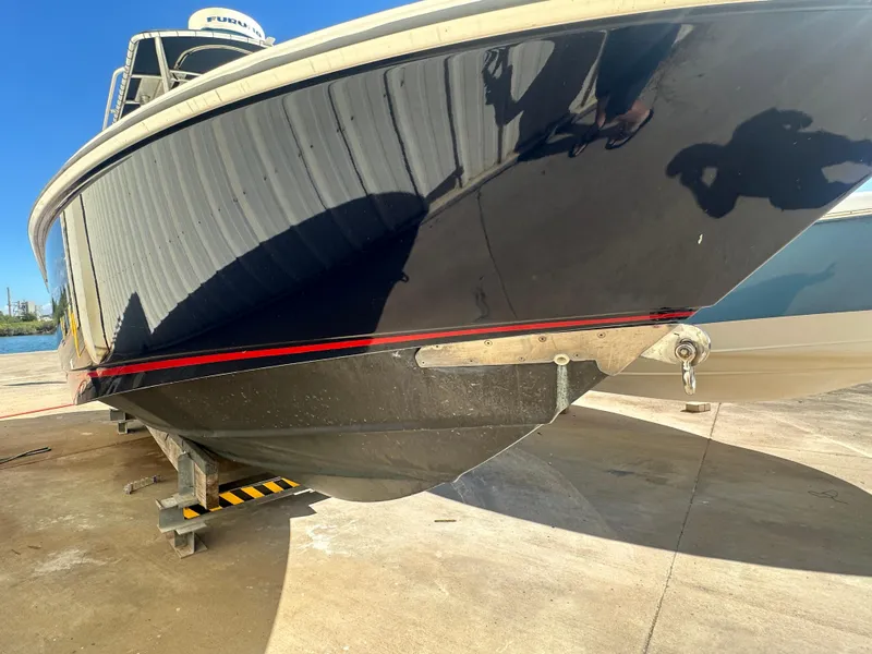 Slide: The Image of 2003 Boston Whaler 270 Outrage boat on dry dock, black hull with red stripe. - 5