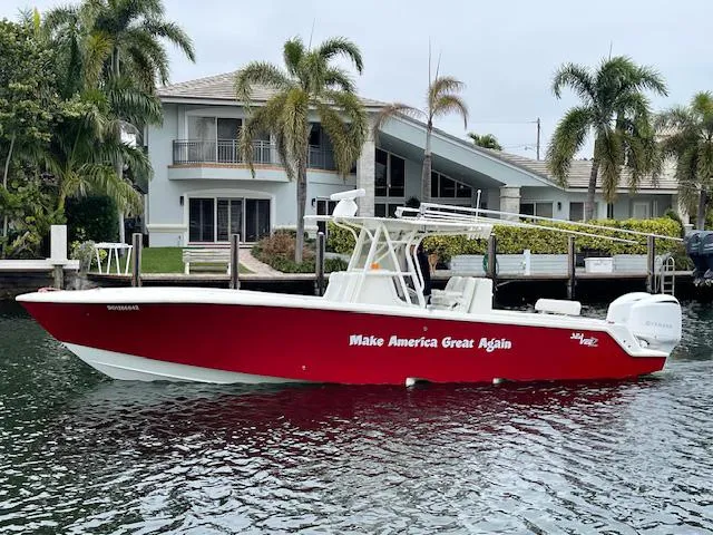 Slide: The Image of 2016 SeaVee 340Z boat with red hull, docked near waterfront home, palm trees in background. - 0