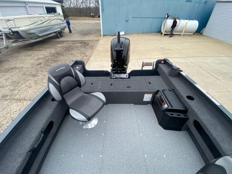 Slide: The Image of 2025 Lund 1775 Pro Guide boat interior with seating and motor, parked outdoors. - 21