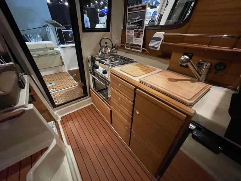 Slide: The Image of 2025 Ranger Tugs R-27 interior kitchen with wooden cabinetry and modern appliances. - 11